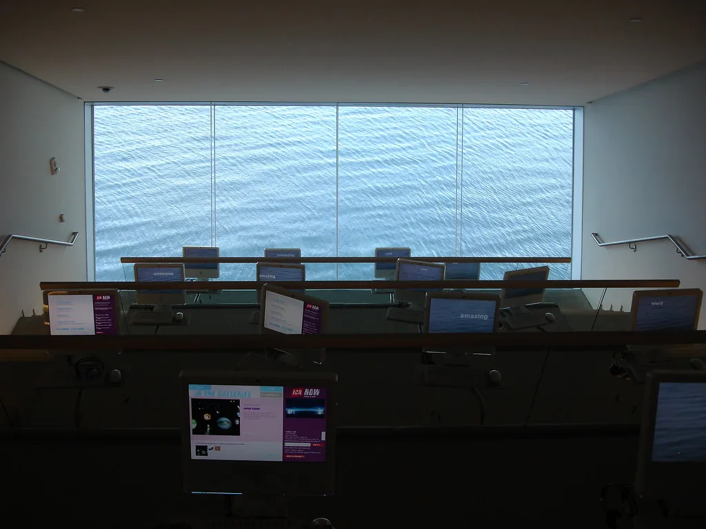 Rangées d'ordinateurs dans une salle sans personne, devant une vitre qui donne sur l'eau